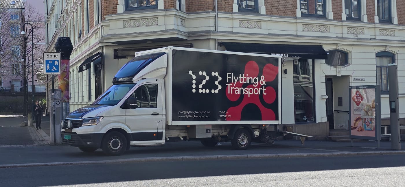 Flyttebil med logoen til 123 Flytting & Transport parkert ved en bygård.